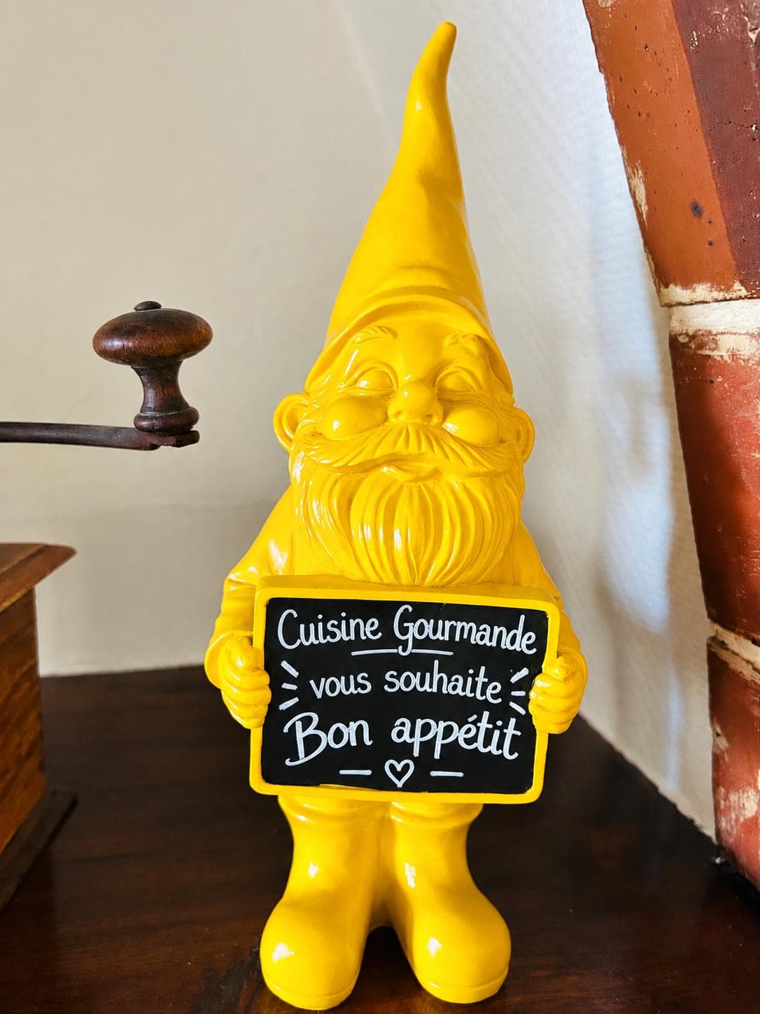 Nain de jardin jaune tenant une ardoise : « Cuisine Gourmande vous souhaite bon appétit »